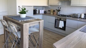 A modern kitchen with white cabinets, a wooden table, and a potted plant. - Stunning Beachfront Apartment on Ferring beach (Ferring)