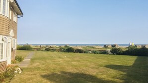 A residential property with a grassy lawn, a pathway leading to the house, and a view of the sea. - Stunning Beachfront Apartment on Ferring beach (Ferring)