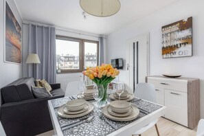 Ein modernes Wohnzimmer mit Essbereich, einer Couch, einem Fernseher und Blick auf die Stadt durch das Fenster.