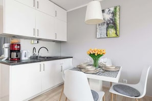 Eine moderne Küche mit weißen Schränken, einer Kaffeemaschine und einem Essbereich mit Tisch für zwei Personen.