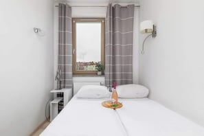 Ein Hotelzimmer mit Bett, einem Vorhangfenster, einem Nachttisch mit Lampe und Blick auf Gebäude.