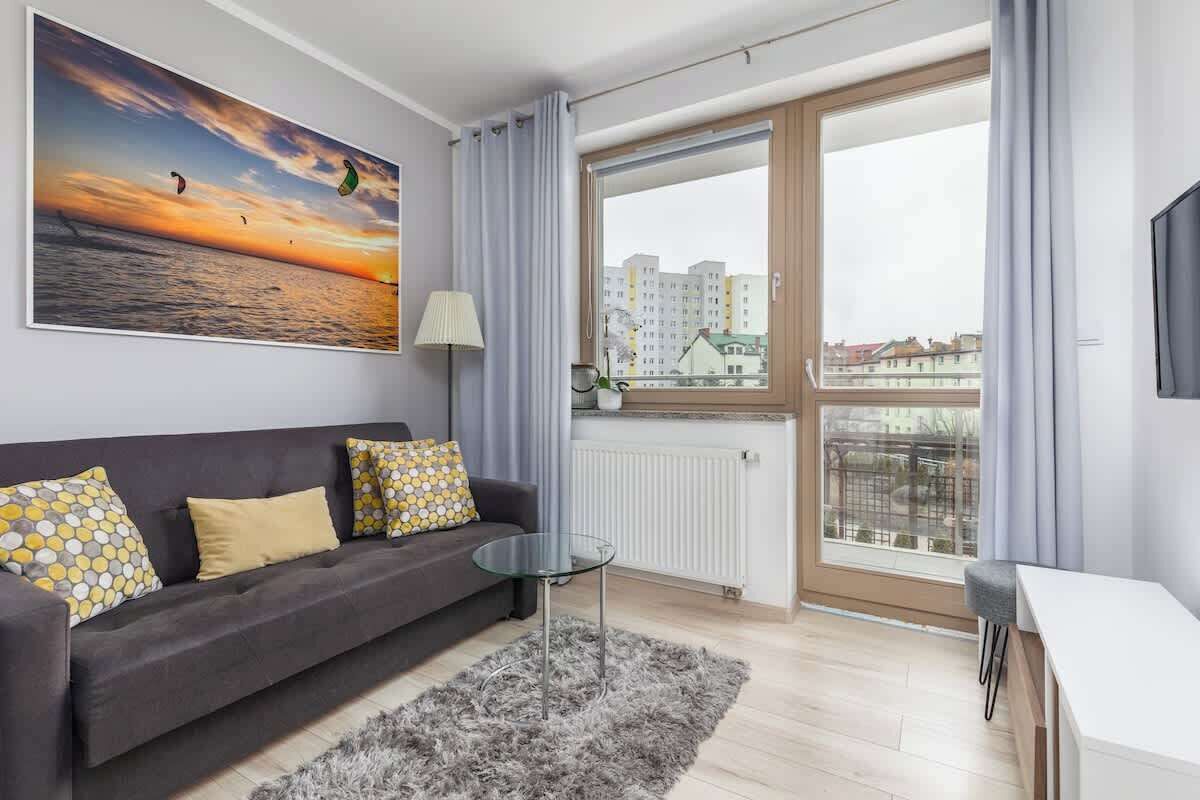 Ein modernes Wohnzimmer mit einer Couch, einem Glastisch und einem großen Fenster mit Blick auf Gebäude.