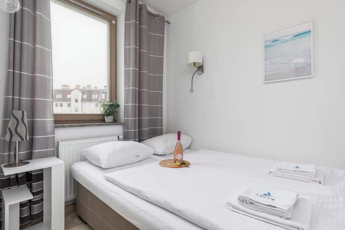 Ein Hotelzimmer mit einem Bett, einem Vorhangfenster, einer Wandleuchte, einer kleinen Topfpflanze und einem gerahmten Bild an der Wand.