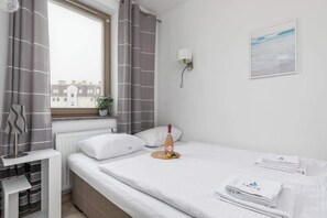 Ein Hotelzimmer mit einem Bett, einem Vorhangfenster, einer Wandleuchte, einer kleinen Topfpflanze und einem gerahmten Bild an der Wand.