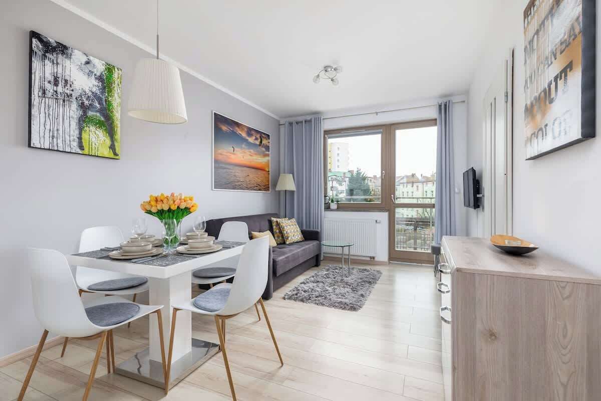 Ein modernes Wohnzimmer mit Essbereich, einem grauen Sofa und einem großen Fenster mit Vorhängen.