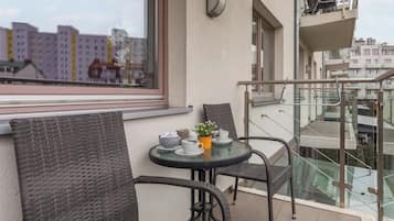 Ein Balkon mit Korbstühlen, einem kleinen runden Tisch mit Tassen und einer Pflanze, und Blick auf andere Gebäude.