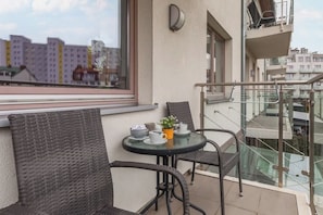 Ein Balkon mit Korbstühlen, einem kleinen runden Tisch mit Tassen und einer Pflanze, und Blick auf andere Gebäude.