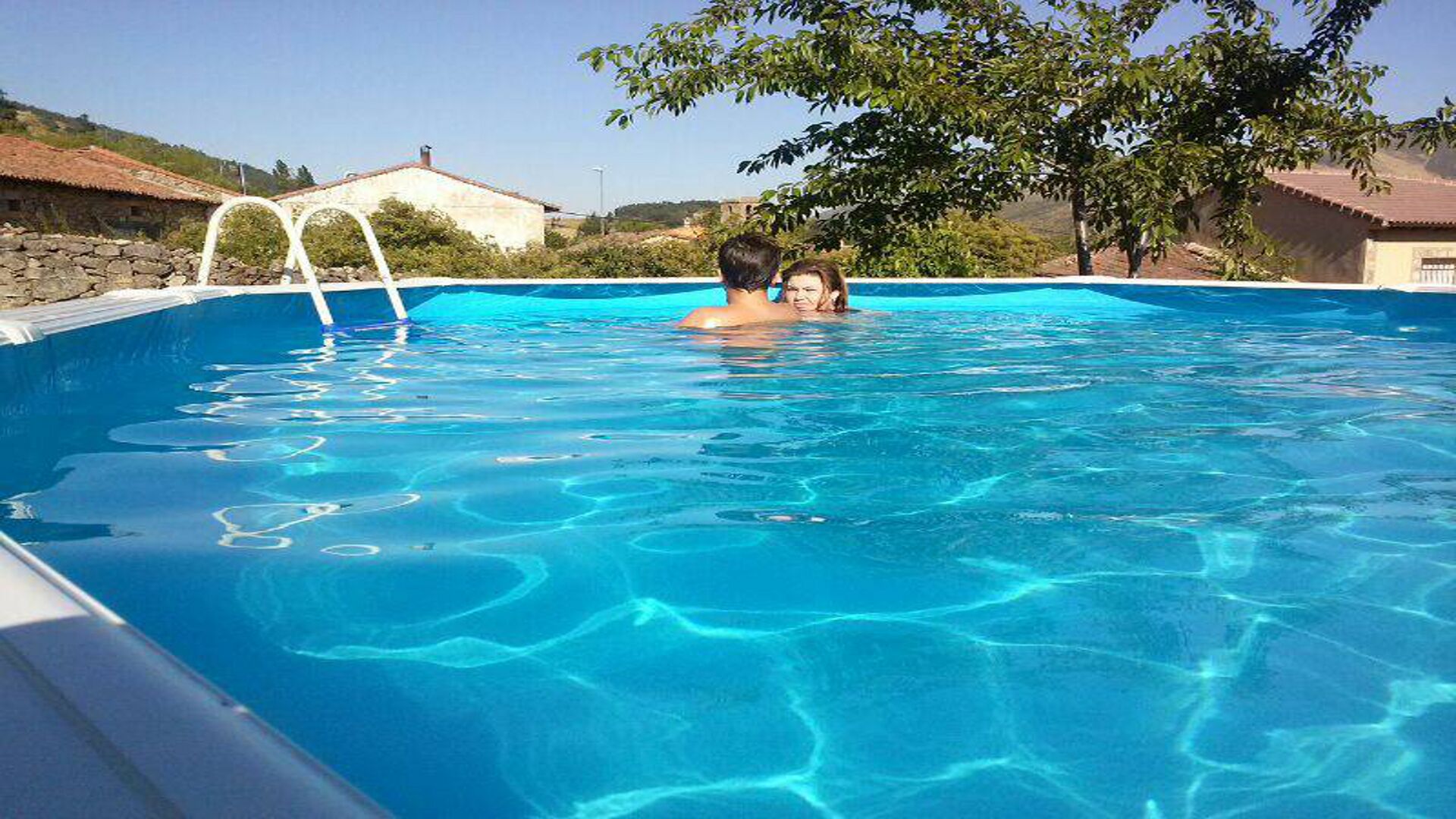 A swimming pool with clear blue water, surrounded by stone walls and trees.