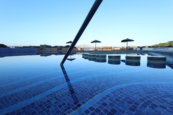 A clear view of a swimming pool with tiled flooring and several umbrellas.
