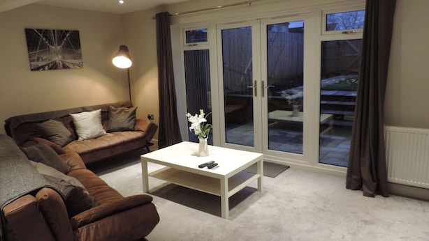 A living room with a brown leather sofa, a white coffee table, and a lamp. - 4 Bedroom Farnborough Airport Accommodation (Hampshire)
