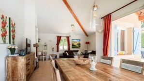 Uma sala de jantar espaçosa com uma mesa de madeira, cadeiras e uma televisão. Há um sofá e um quadro na parede.