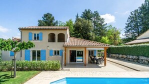 Uma casa de dois andares com piscina, varanda coberta e jardim.