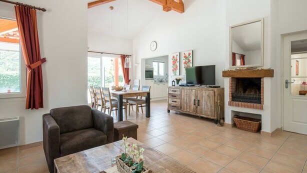 Uma sala de estar ampla com lareira, área de jantar e cozinha ao fundo.