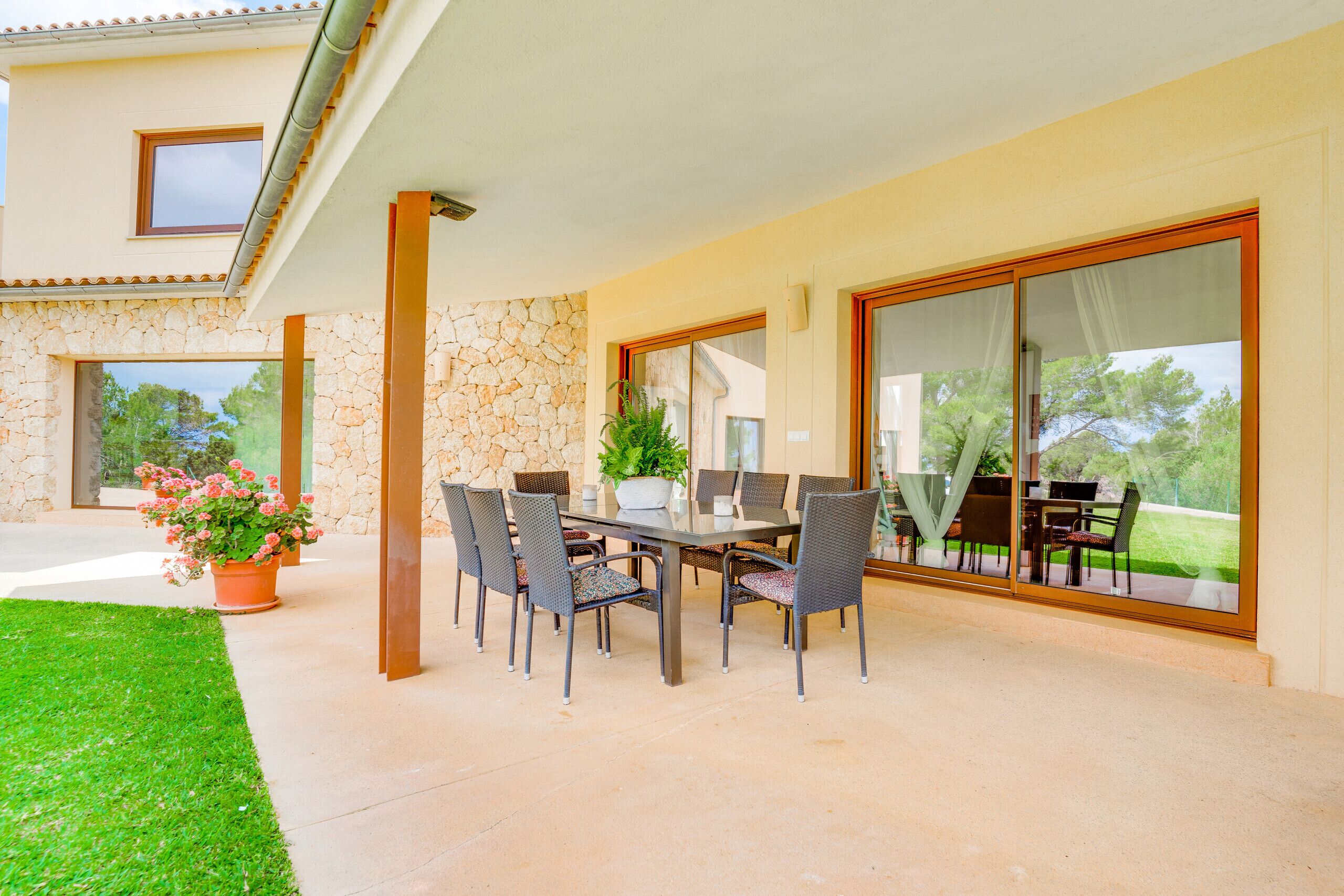 An outdoor patio with a dining table and chairs, a potted plant, and a stone wall.