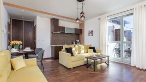 Una sala moderna con sofá, mesa de centro y comedor. Se observa una cocina al fondo con armarios de madera y una ventana con vista a un balcón.