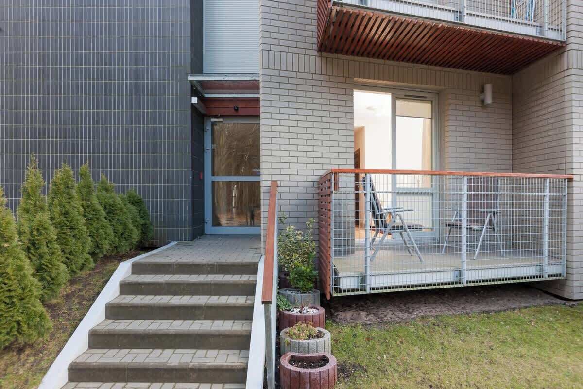 En modern byggnad med en fasad av tegel, en trappa av betong som leder upp till en dörr och ett inhägnat utomhusområde med ett bord och stolar.