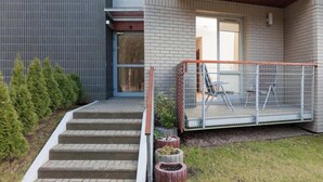 Un edificio moderno con fachada de ladrillo, una serie de escalones de hormigón que llevan a una puerta y un área exterior cercada con una mesa y sillas.