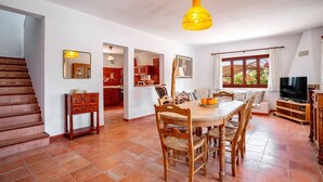 Amplia sala de estar con una mesa de comedor de madera, sillas, un televisor y una escalera.