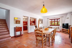 A spacious living area with a wooden dining table, chairs, a TV, and a staircase.