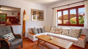Una sala de estar con un sofá, una mesa de madera, una silla, una lámpara y una ventana con cortinas.