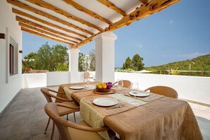 A covered outdoor dining area with a table set for four, surrounded by wicker chairs, under a wooden pergola.