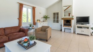 Ein Wohnzimmer mit braunem Ledersofa, einem beige farbenen Sessel, einem weißen Couchtisch mit Dekoration, einem Fernseher auf einem weißen Schrank und einem Kamin.