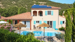 Ein zweistöckiges Haus mit Swimmingpool, Sitzgelegenheiten im Freien und Blick auf einen Hügel.