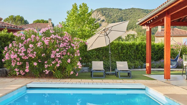 Ein Swimmingpool mit Liegestühlen und Sonnenschirm, umgeben von viel Grün und Blick auf Hügel.