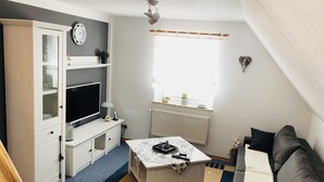 Kompakti olohuone, jossa on televisio, valkoiset huonekalut, ikkunasta avautuva näkymä ja patteri.