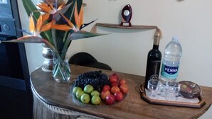 Une table en bois sur laquelle se trouvent un panier de fruits, une bouteille d’eau, une bouteille de vin et une plante décorative.