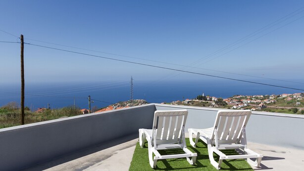Deux fauteuils de jardin blancs sur une terrasse sur le toit, avec vue sur la mer et une ville lointaine.