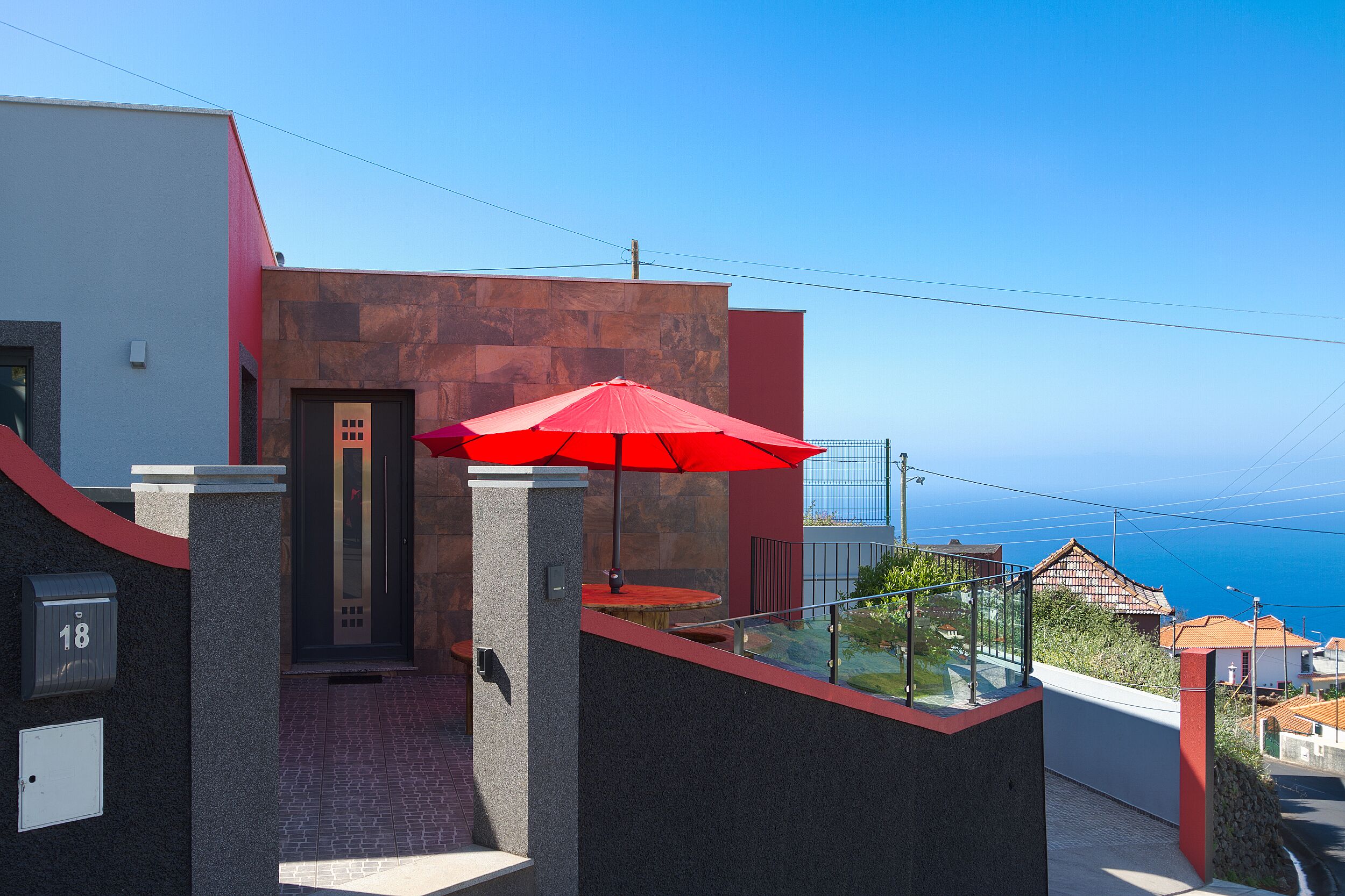 A modern building with a red umbrella, a stone facade, and a view of the sea.