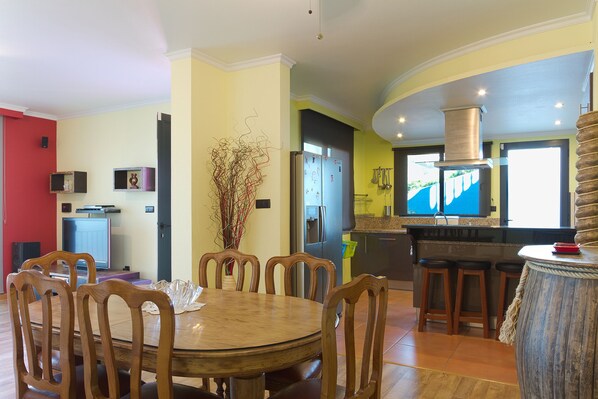 A modern kitchen with a dining area, featuring a round wooden table, bar stools, and a built-in stove.
