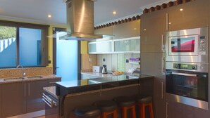 Une cuisine moderne dotée d’appareils électroménagers en acier inoxydable, d’un grand îlot central avec des tabourets de bar et d’une fenêtre offrant une vue sur l’extérieur.
