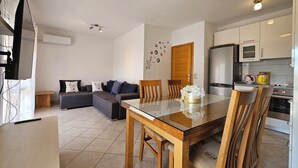 Una sala de estar moderna con un sofá, una mesa de comedor con sillas, un televisor y una cocina con electrodomésticos.