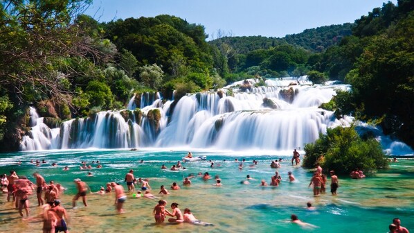 Een waterval met meerdere niveaus, omgeven door weelderige begroeiing en helder turquoise water.