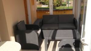 A sunlit patio with a sofa set, two armchairs, and a small table. - Detached house "Chez Jean-Yves" with veranda and garage  (Le Menil)