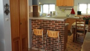 A kitchen with a brick backsplash, wooden cabinets, and a bar area with two stools. - Detached house "Chez Jean-Yves" with veranda and garage  (Le Menil)
