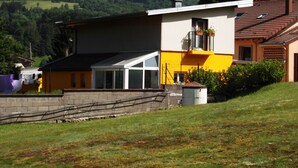 A modern two-story house with a large balcony, a conservatory, and a view of a forested hill. - Detached house "Chez Jean-Yves" with veranda and garage  (Le Menil)