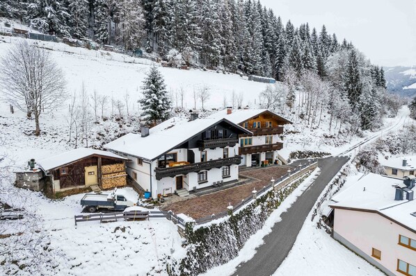 Un village de montagne enneigé, avec ses maisons traditionnelles en bois, une route pavée et une vue dégagée sur la forêt environnante.