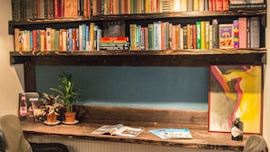 Un rincón acogedor para leer con un banco de madera, dos sillones a rayas, una estantería llena de libros y un cuadro abstracto y colorido.