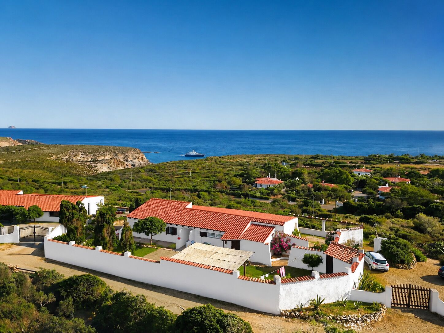 A coastal property with white buildings, red-tiled roofs, and a view of the sea.