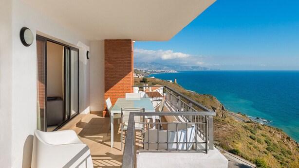A balcony with a table and chairs, overlooking a coastal view. - 2 bedroom apartment front sea view (Torrox Costa)