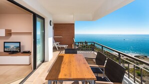 A balcony with a wooden table and chairs, a TV, and a view of the sea. - 2 bedroom apartment front sea view (Torrox Costa)