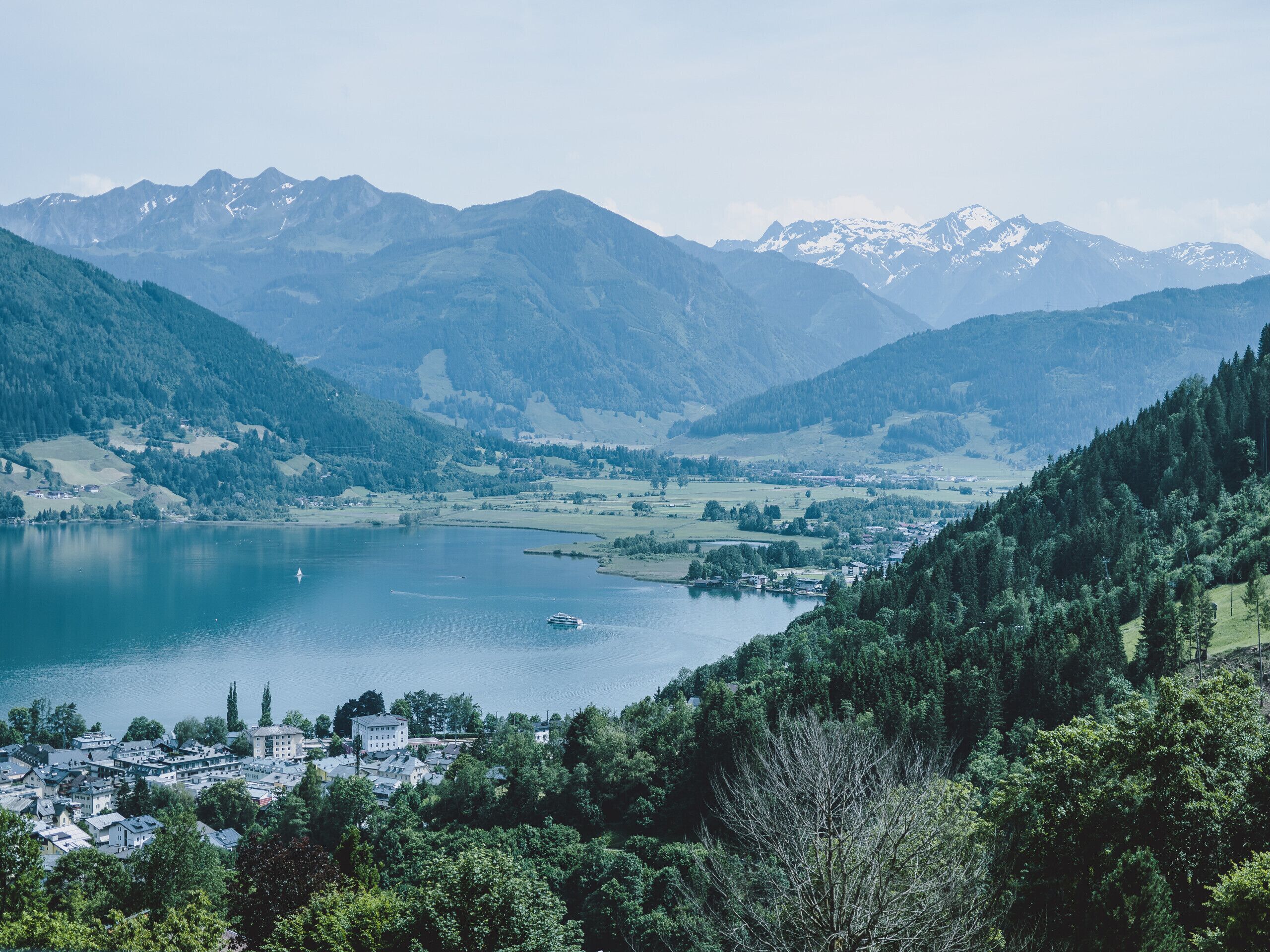 A lakeside town with buildings, a boat on the lake, and mountains in the background.