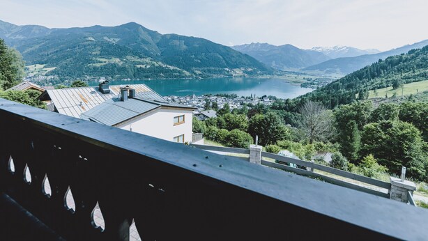 Una vista panorámica de un lago rodeado de montañas, con un pueblo en primer plano y un balcón con vistas al paisaje.