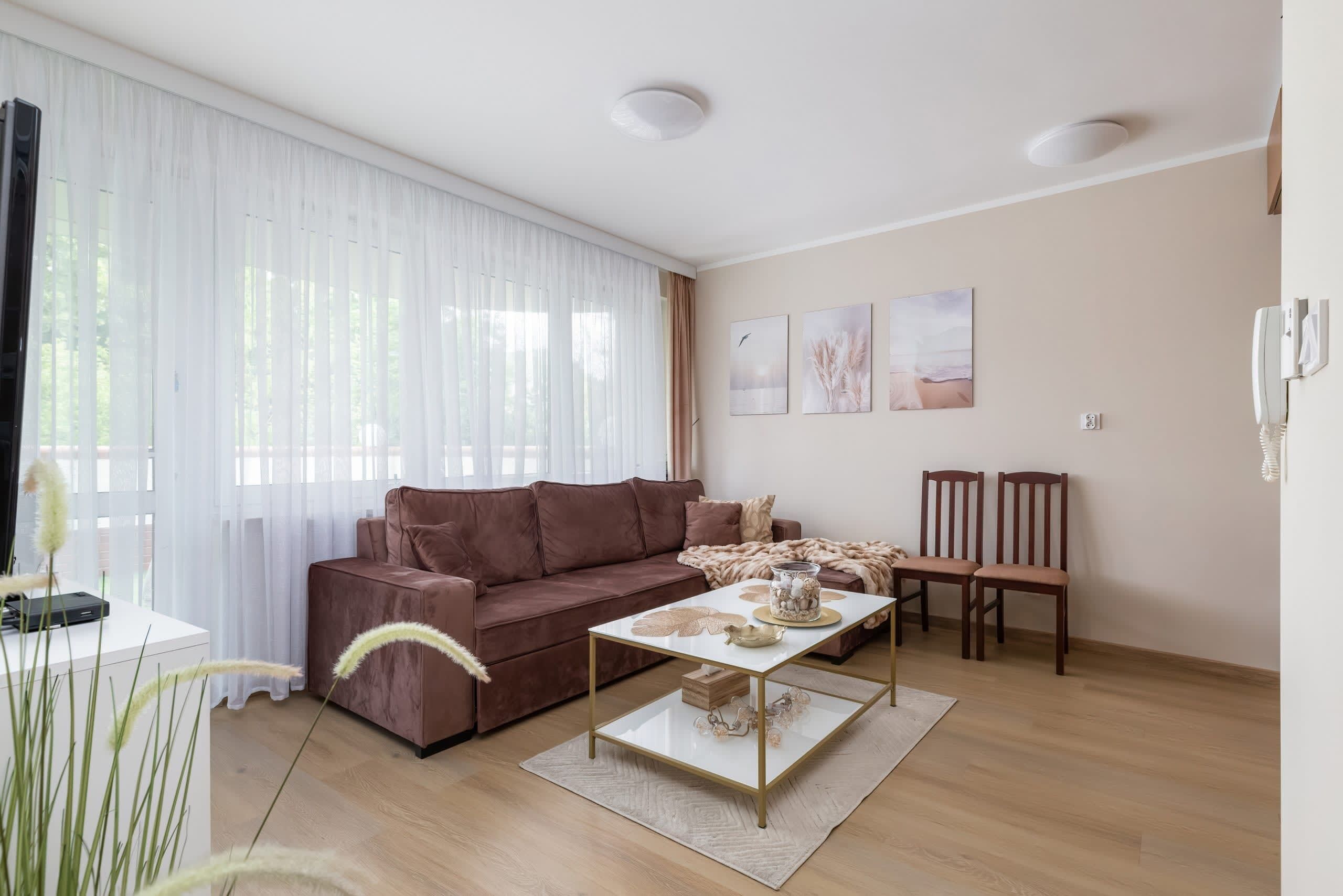 A living room with a brown sofa, a coffee table, and two chairs. There are three wall-mounted pictures and a telephone on the wall.