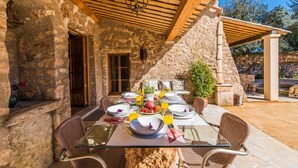 Un espace extérieur aménagé pour les repas, avec des murs en pierre, des poutres en bois et des chaises en osier.