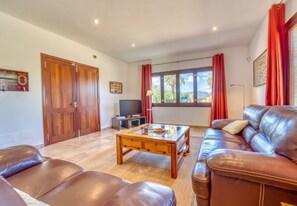 A living room with leather sofas, a wooden coffee table, a TV, and a large window with curtains.