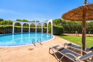 A swimming pool with a white pergola structure, lounge chairs, and a thatched umbrella.